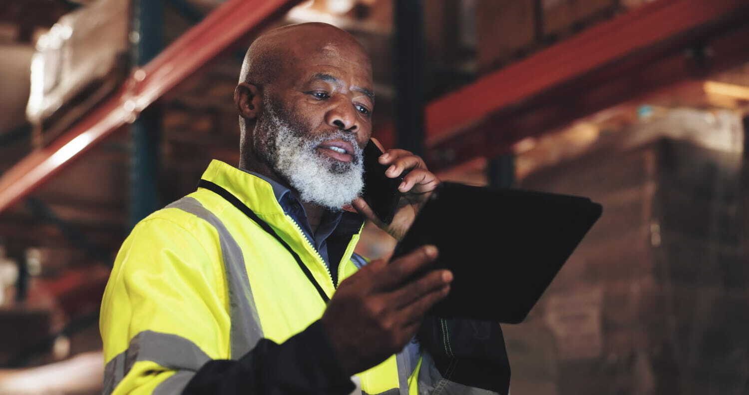 Operator in a high-visibility jacket on the phone, with a tablet, in a warehouse